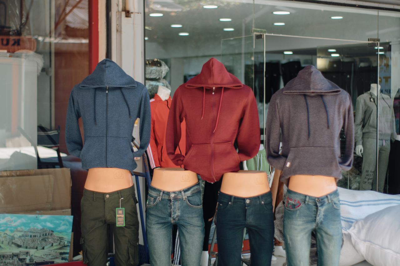 Hooded sweatshirts and jeans displayed on mannequins in a retail storefront window.